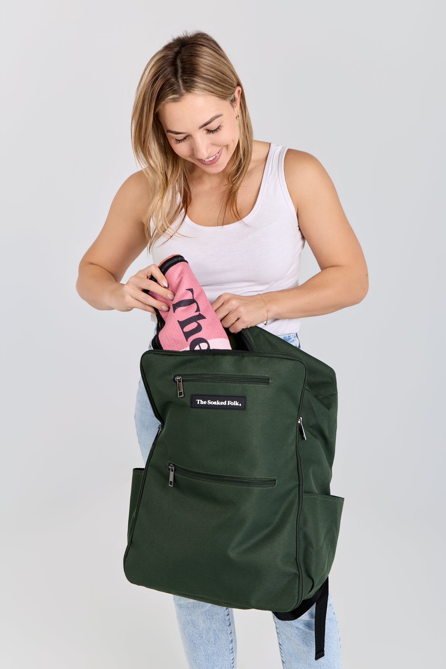 Woman holding a green backpack with a pink item inside on a light gray background
