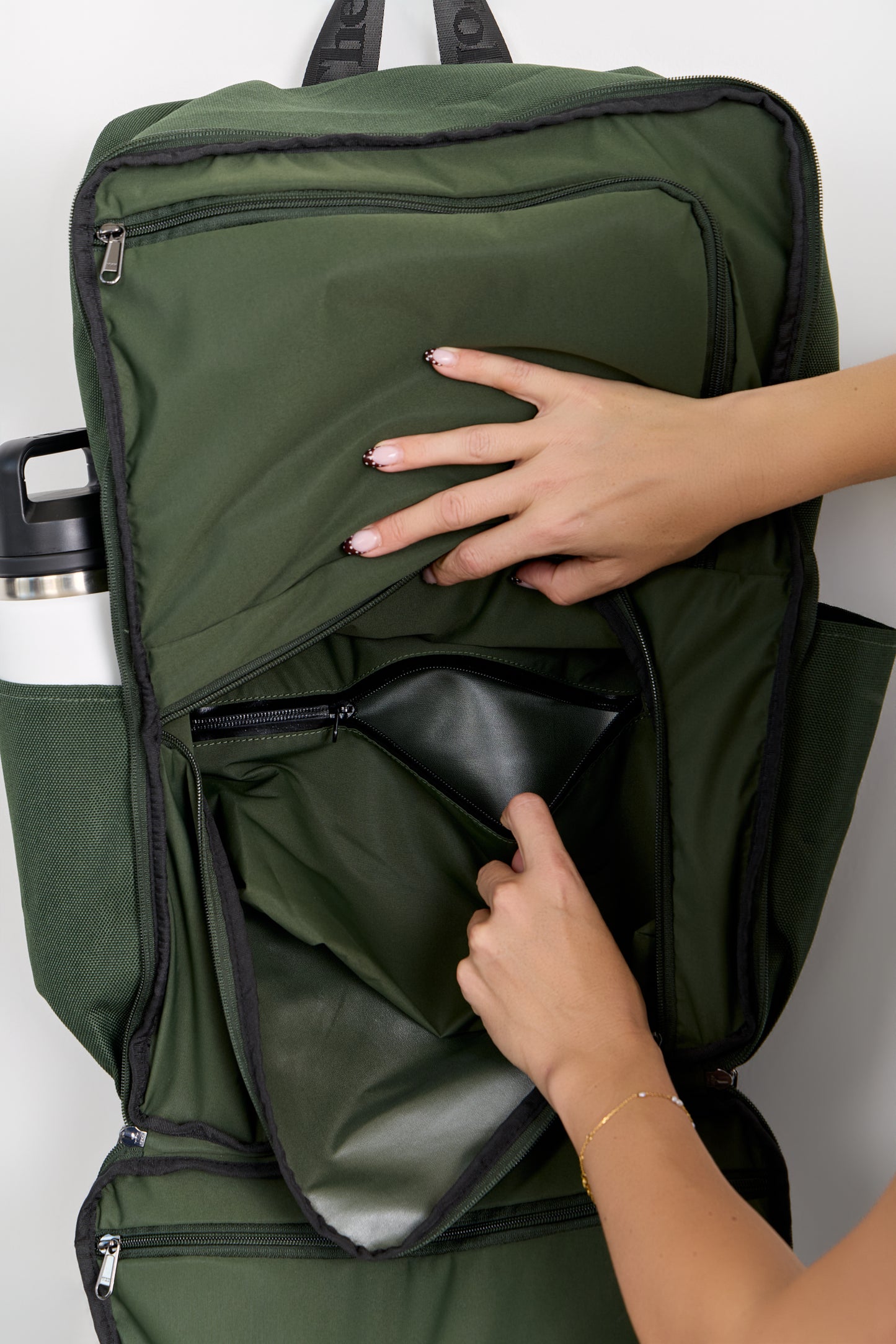 Green backpack with a hand opening a compartment on a white background