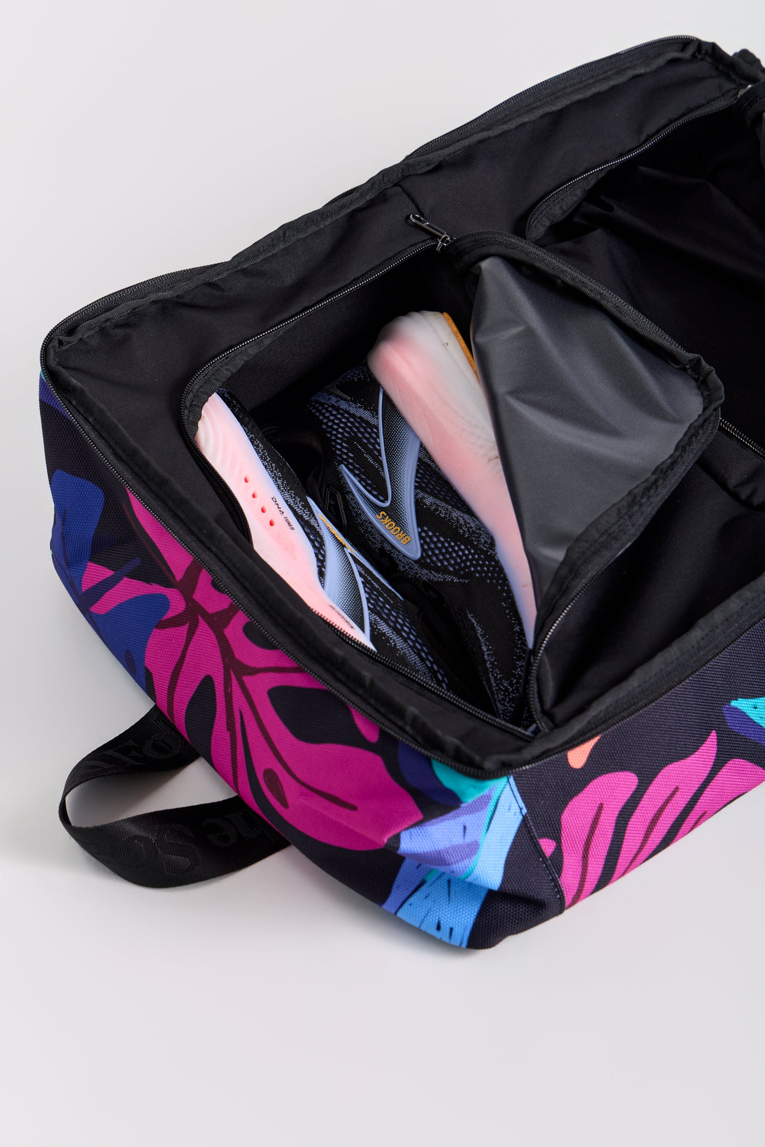 Black backpack with colorful leaf pattern containing a pink and black sneaker on a light gray background